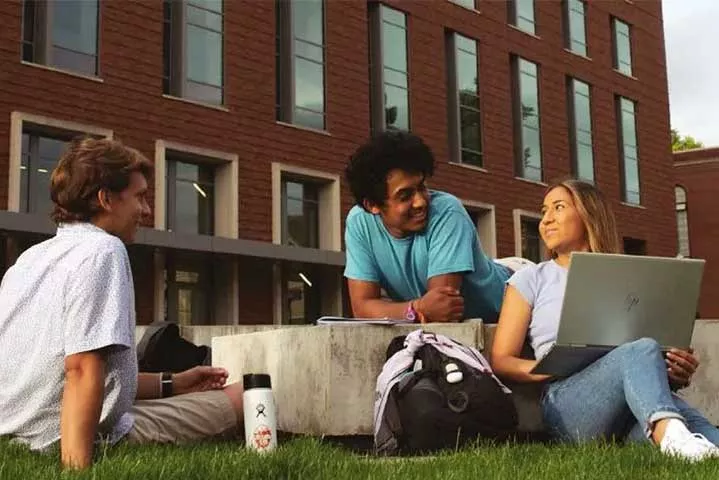 three students with bags and laptops talking outside