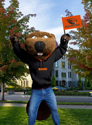 Benny on campus with fall trees in background holding an OSU flag