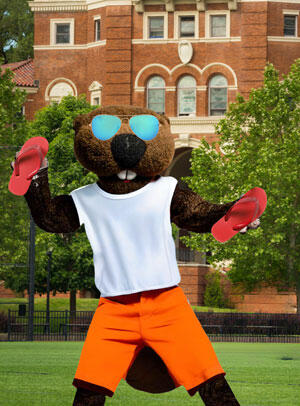 Benny on campus wearing a tank and board shorts holding flip flops
