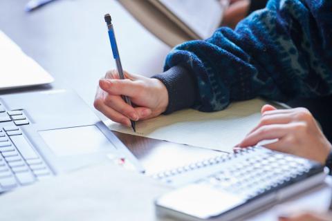 Hands writing notes in front of a laptop